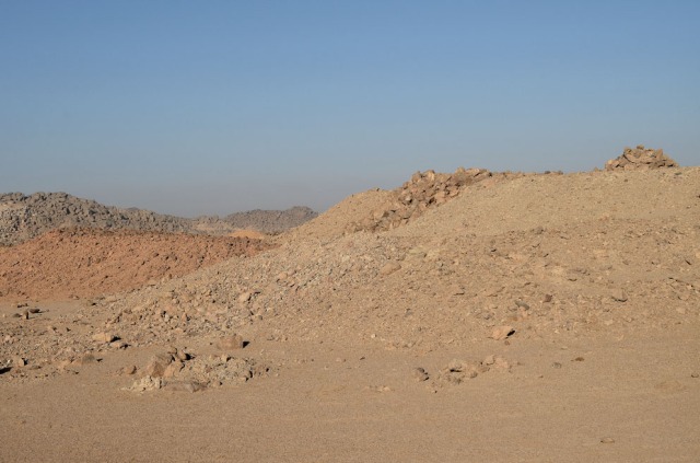 Different types of spoil heaps at site 9 in Wadi el-Hudi: At the left is a “red” heap, originating from a place in the mine with particularly red granite, in the middle is a mixed heap from the main part of the mine, in the background are large stone blocks from this mine, as well as fine debris at the top. The latter is a workplace for splitting amethyst from quartz. Photo by Per Storemyr